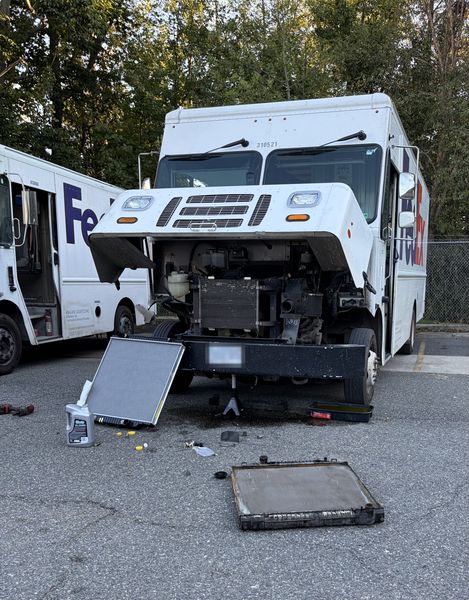 Step van with the front hood open and the old radiator on the ground beside the new one
